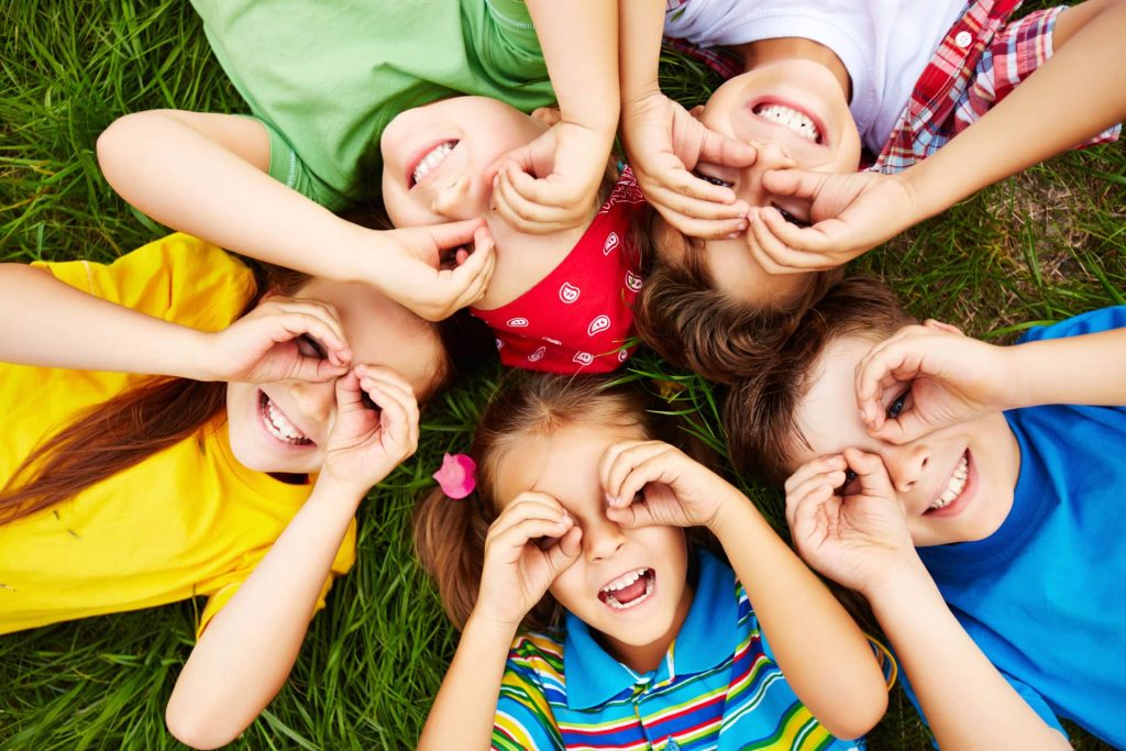 Spielende Kinder mit Handbrillen liegen im Gras